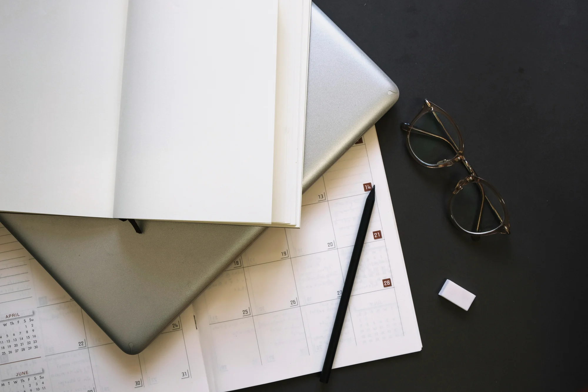 Cuaderno, calendario, portátil y gafas sobre una mesa de despacho