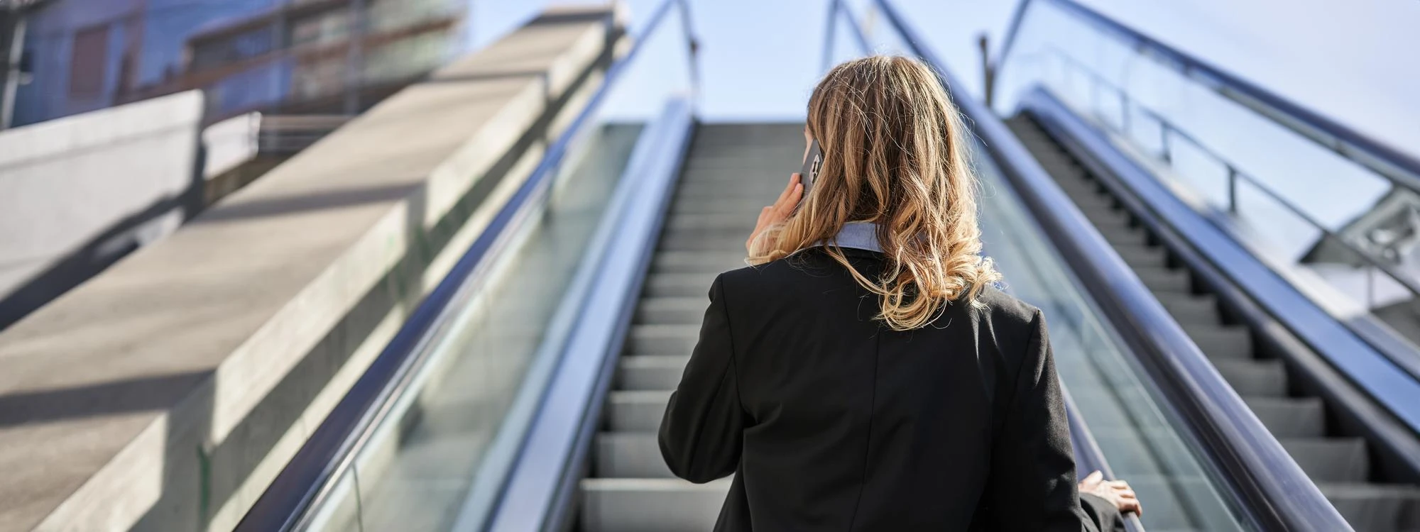 Directiva de espaldas subiendo unas escaleras mecánicas en un edificio corporativo